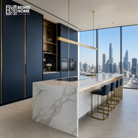 Meubles de cuisine contemporains bleu marine, îlot cascade en pierre frittée Statuario, éclairage linéaire en laiton, menuiserie sur mesure pour penthouse