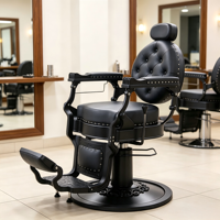 Chaise de coiffure noire gothique, cuir capitonné rond, accoudoirs en métal mat et base circulaire sur pied.