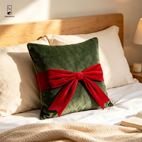 Coussin carré décoratif en velours vert foncé avec nœud rouge, idéal pour les fêtes de Noël et l'ambiance festive à la maison