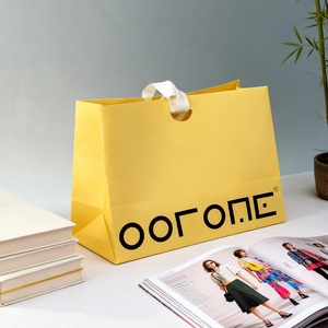 حقيبة ورقية صفراء زاهية بخط أسود جريء، تتميز بمقابض بيضاء متينة، تم التقاطها في نمط حياة بسيط - Product Image 2