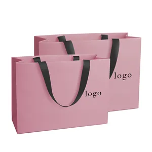 Tas kertas belanja logo kustom merek mewah untuk pakaian pink matte pakaian pakaian butik tas kemasan dengan pegangan pita