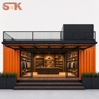 Conteneur modulaire de vente au détail pour boutique éphémère, avec volumes empilables, pavés gris pierre, jardinières noires, sièges extérieurs et espace photo