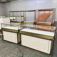 Vitrina de Joyería Rectangular de Vidrio de Lujo con Marco de Metal Dorado, Pedestal Blanco y Luz LED Flotante para Boutique Minorista