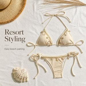 Bikini de mujer con parte inferior de tanga acanalada, ribete de encaje y dijes de concha, color beige. - Product Image 1