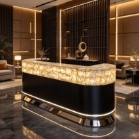 Comptoir de réception en pierre naturelle rétroéclairée, quartz blanc cristallin, translucide et lumineux, avec base noire mate et finition métallique.