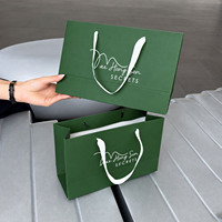 Sac cadeau en papier vert forêt de luxe avec logo blanc minimaliste et poignées en ruban doux pour l'emballage de produits de soin et de cosmétiques