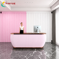 Bureau d'accueil rose moderne avec façade cannelée verticale, finition or rose, comptoir foncé et intérieur de hall de luxe contemporain