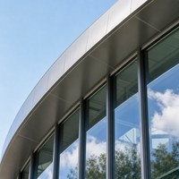 Bâtiment d'exposition moderne en acier avec façade entièrement vitrée, poutres de toit hautes et place d'accueil publique