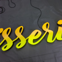 Enseigne LED personnalisée avec police artistique aux couleurs vives, finition UV et base en acier inoxydable noir, pour diverses devantures de magasins et vitrines