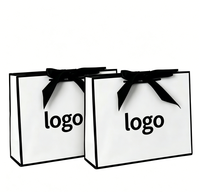 Sac en papier cadeau blanc de luxe recyclable en gros d'usine avec nœud en ruban noir et logo personnalisé pour l'emballage de vêtements et d'artisanat de détail