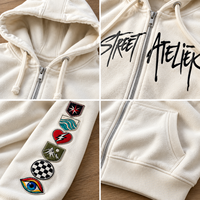 Sweat à capuche oversize crème zippé avec imprimé graphique sur la poitrine, patchs brodés sur les manches, épaules tombantes, style streetwear, personnalisable, vente en gros