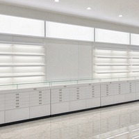 Système d'affichage mural pour lunettes en laque blanche avec étagères LED lumineuses et comptoir à tiroirs pour l'aménagement de magasins d'optique