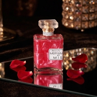 Son flacon de parfum carré à capuchon multifacettes, col doré, liquide nacré, étiquette bleue rubis, radiant, romantique, longue durée