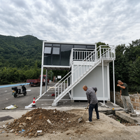 Maison conteneur démontable à deux niveaux, module en acier, panneau ondulé noir, escalier blanc, terrasse pour camp de terrain rural ou bureau