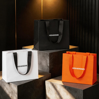 Sac de luxe pour vêtements en papier spécial noir jais avec logo blanc, structure en C inversée monochrome, idéal pour offrir des vêtements haut de gamme