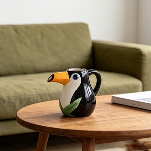 Pichet en céramique en forme de <span class=keywords><strong>toucan</strong></span> avec <span class=keywords><strong>bec</strong></span> orange, yeux bleus et détails de feuilles vertes pour cuisine tropicale, idéal pour café, lait ou eau - Product Image 1