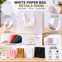 Sac en papier cadeau blanc de luxe recyclable en gros d'usine avec nœud en ruban noir et logo personnalisé pour l'emballage de vêtements et d'artisanat de détail