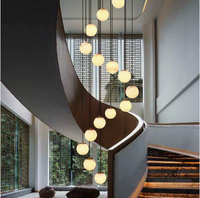 Lustre moderne en spirale pour escalier long, avec boules en albâtre naturel et structure métallique, idéal pour villa et hall à plafond haut