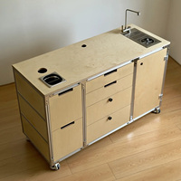 Meuble de cuisine mobile en profilé aluminium et contreplaqué marin, avec évier, tiroirs et roulettes, servant également de bar à café et d'îlot.