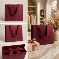 Sac en papier de luxe bordeaux à motif gaufré avec poignée en ruban gros-grain et nœud décoratif pour boutique de vêtements