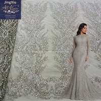 Tissu en dentelle brodée de perles et de sequins en cristal argenté sur maille avec bord festonné pour robe de mariée ou de soirée