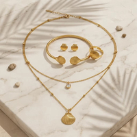 Parure de bijoux hypoallergénique en acier inoxydable plaqué or, comprenant un collier double coquille, des boucles d'oreilles puces et un bracelet ajustable à ouverture.