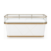 Comptoir de présentation de bijoux en verre avec corps laqué blanc, bandes décoratives dorées et façade géométrique pour boutique de détail
