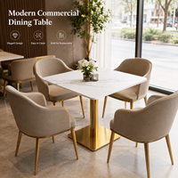 Table et chaises de restaurant, plateau carré en pierre frittée avec base cylindrique dorée et fauteuils beiges à accoudoirs en forme de baril pour café-bar