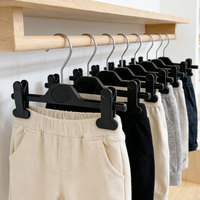 Vente en gros directe usine : Cintre pour pantalons d'enfants en plastique noir avec crochet pivotant en métal et pinces antidérapantes fixes, personnalisable