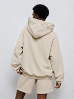 Sweat à capuche homme streetwear coupe ample en molleton de coton épais, avec motif graphique brodé beige personnalisé et manches brodées style script, tendance