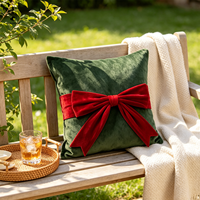 Coussin carré décoratif en velours vert foncé avec nœud rouge, idéal pour les fêtes de Noël et l'ambiance festive à la maison