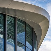 Salle d'exposition industrielle en acier avec mur-rideau en verre haut, structure de toit et grande place publique