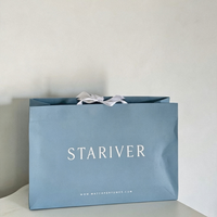 Sac cadeau en papier bleu poussière mat avec ruban en satin blanc et poignée à nœud, logo personnalisé en serif, sac de luxe pour boutique de parfums