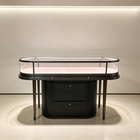 Comptoir d'exposition d'îlot commercial noir mat personnalisé avec table en verre, incrustation rose, éclairage LED, tiroir pour montres et vitrine ovale pour bijoux