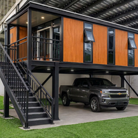 Maison conteneur surélevée à deux étages avec garage, finition bois laminé, structure en acier noir, terrasse vitrée du sol au plafond