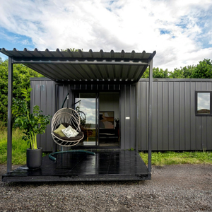 Maison préfabriquée en conteneur avec porte coulissante en verre, cabane modulaire extérieure en acier, cadre en aluminium noir, terrasse et chaise suspendue - Product Image 1