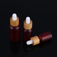 Botol Tetes Kaca Merah Buram dengan Logo Kustom Profesional dan Tutup Bambu untuk Penyimpanan Minyak Esensial Kosmetik Merek Kecantikan.