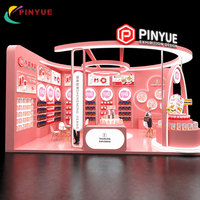 Stand d'exposition moderne rose et blanc avec arches LED incurvées, comptoir de présentation à niveaux, étagères rétroéclairées, bureau d'accueil et espace de réunion