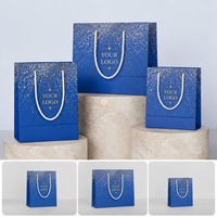 Sac de courses en papier écologique de luxe bleu foncé avec impression personnalisée effet éclaboussures d'or, logo sérigraphié sur corde, pour boutique de vêtements et cadeaux