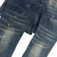 Pantalon slim en denim bleu vintage pour homme, style streetwear automne, avec patch logo au dos, détails déchirés et tissu froissé