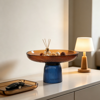 Twee-kleurige glazen fruitschaal, amberkleurige plaat met blauwe geribbelde voet, moderne decoratieve serveerschaal op voet voor thuis op tafel.