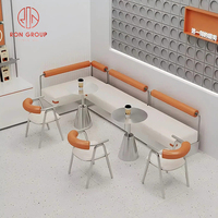 Ensemble de mobilier de restaurant commercial, canapé en cuir blanc en forme de L, tables rondes en métal, chaises orange pour la restauration et l'hôtellerie