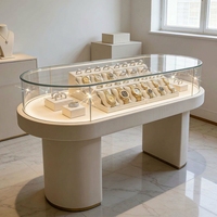 Moderner Cremeweißer Ovaler Schmuck-Präsentationstisch LED-Beleuchtete Glasvitrine für Einzelhandels-Schmuckgeschäfte