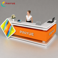Comptoir de réception personnalisé orange pour le commerce de détail avec logo LED, plateau blanc et panneau latéral coloré pour centre commercial, hall d'entreprise, vente directe usine
