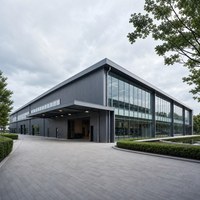 Grande structure de centre d'exposition en acier avec poutres de toit apparentes, entrée en verre et espace de réception paysagé pour événements