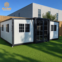 Maison préfabriquée portable à double aile extensible avec panneaux extérieurs foncés, structure blanche et plan d'aménagement ouvert pour une habitation temporaire