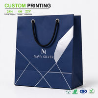 Sac en papier bleu marine imprimé sur mesure avec marquage argenté et poignée en cordon tressé pour l'emballage de voyage et de vente au détail en boutique, vente en gros
