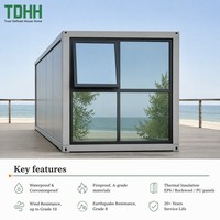 Maison conteneur TDHH avec panneaux gris, mur latéral entièrement vitré, cadre foncé et transom