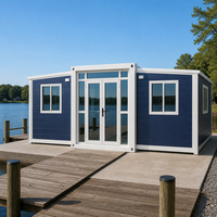 Maison conteneur pliable extensible bleu foncé à bardage horizontal avec portes et fenêtres latérales en verre pour le glamping en bord de lac