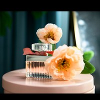 Parfum pour femme en verre côtelé carré avec capuchon argenté, ruban rose, liquide ambré, bouquet doux, pétales romantiques, longue tenue
